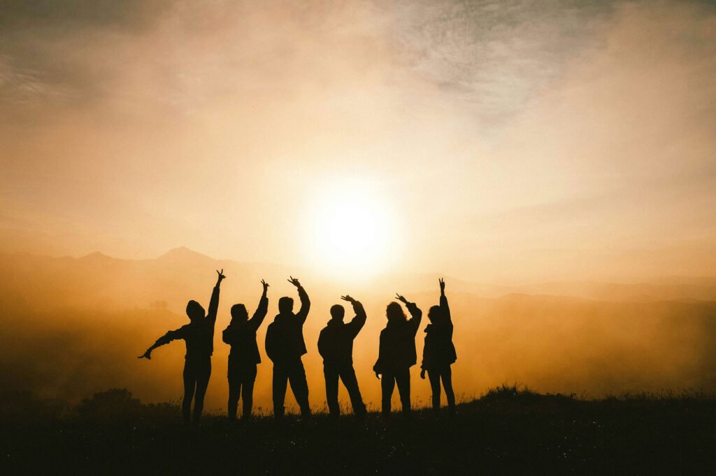 silhouette of six people with raised hands watching sunset.