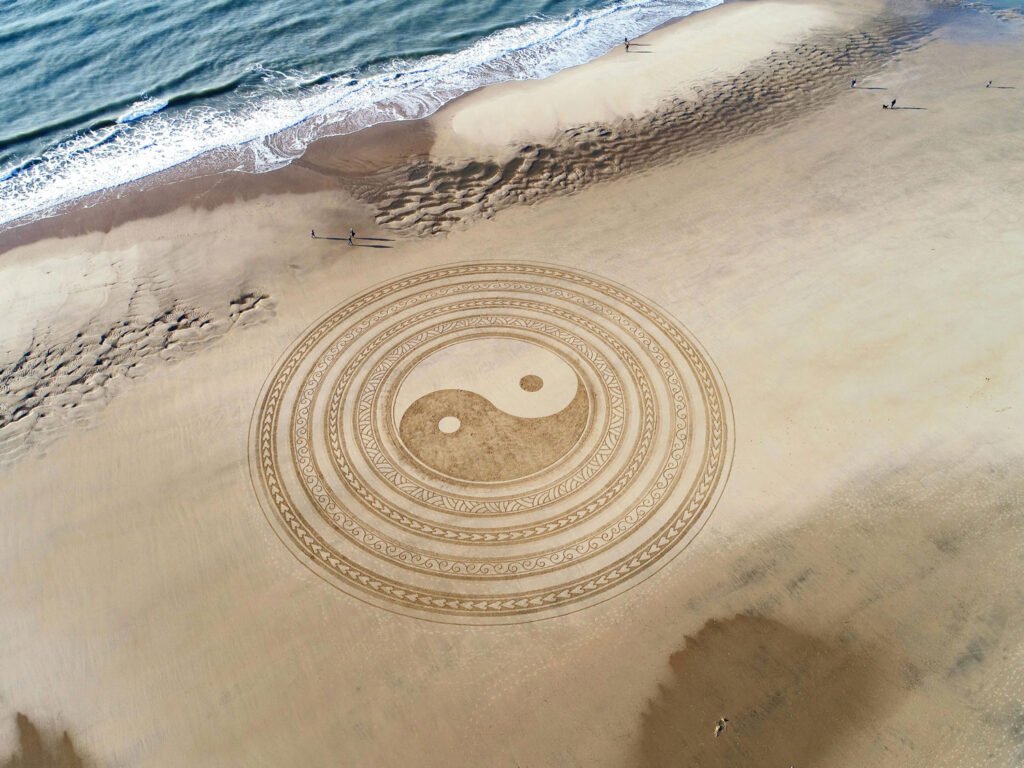 beach with a drawing in the sand of a ying yan.