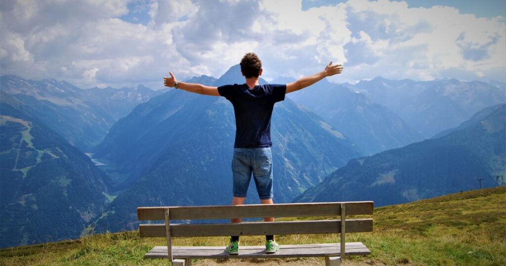 Man with open arms facing mountain landscape